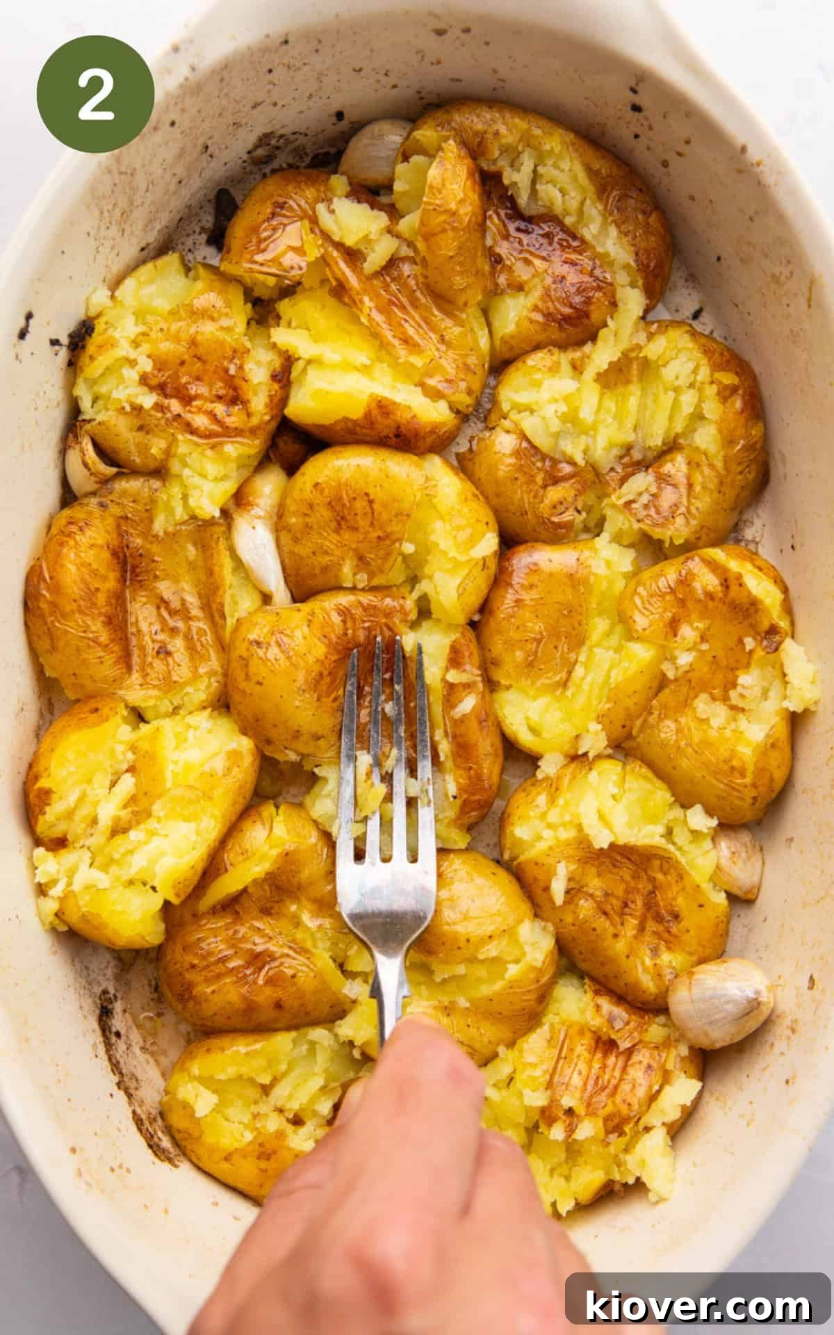 Smashed potatoes being flattened with a fork on a baking sheet.