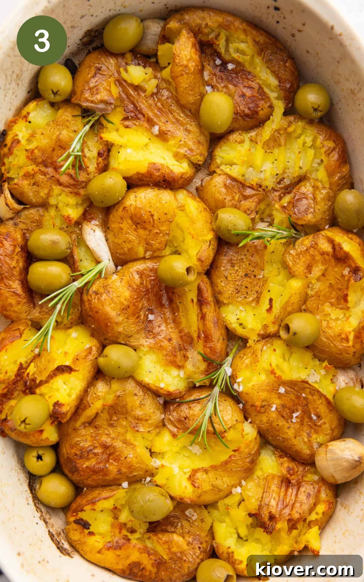 Adding olives and fresh herbs to the crispy smashed potatoes after the final bake.