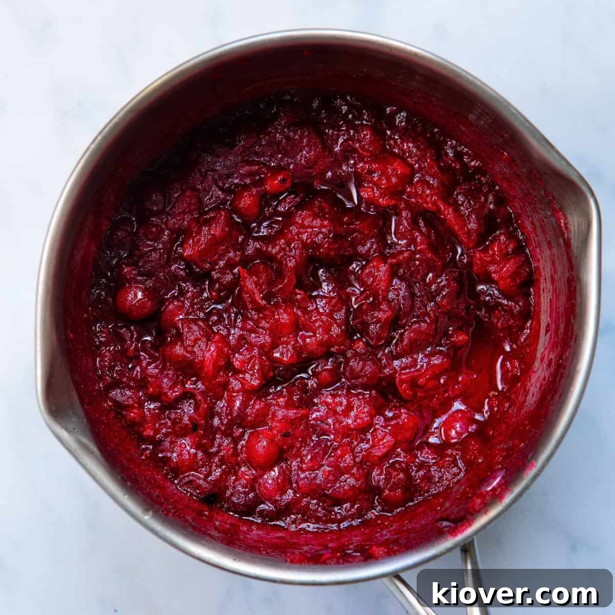A saucepan filled with freshly made homemade cranberry sauce, vibrant red and slightly chunky.