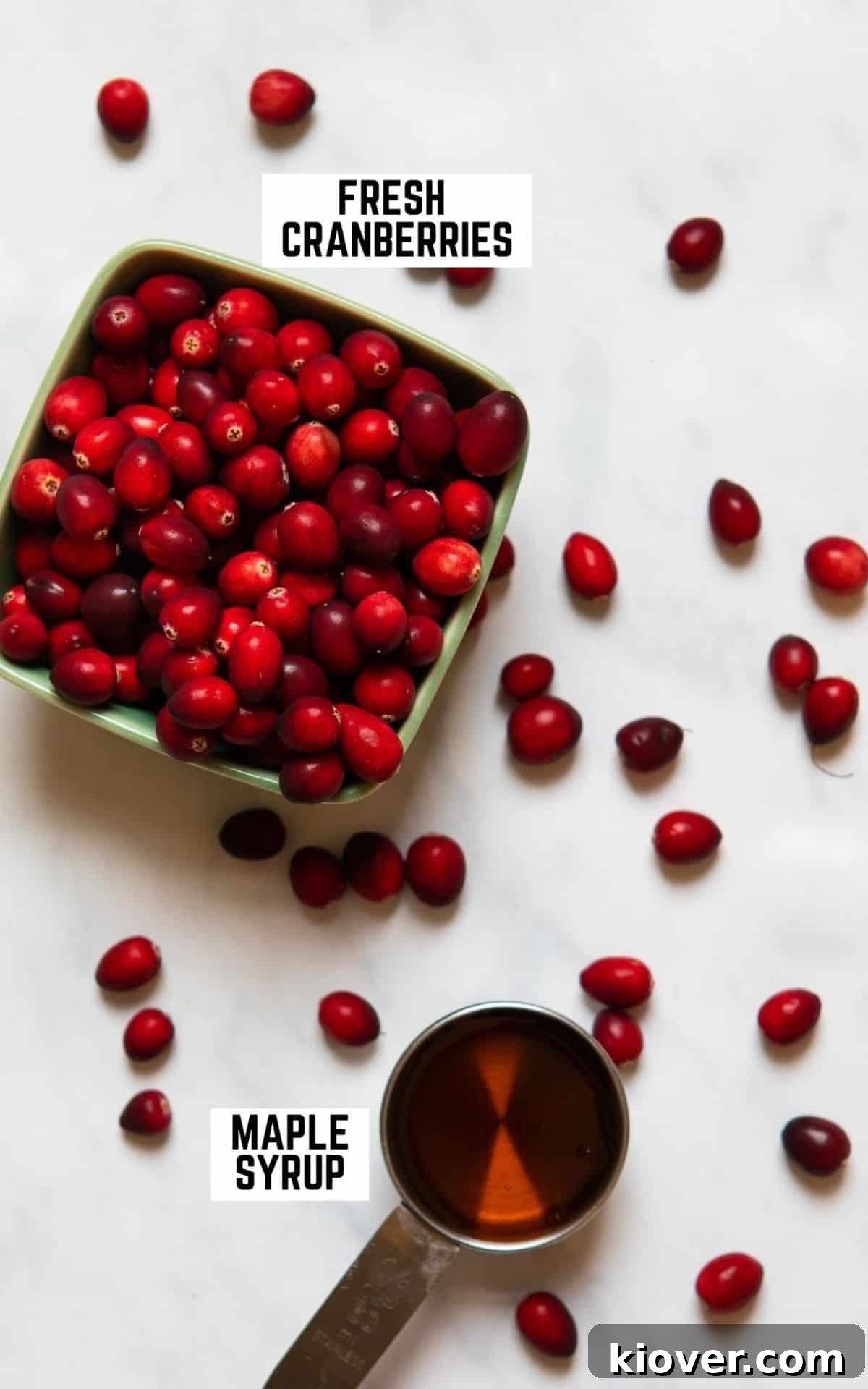 Fresh cranberries and a bottle of maple syrup arranged on a white background, representing the two main ingredients for the sauce.
