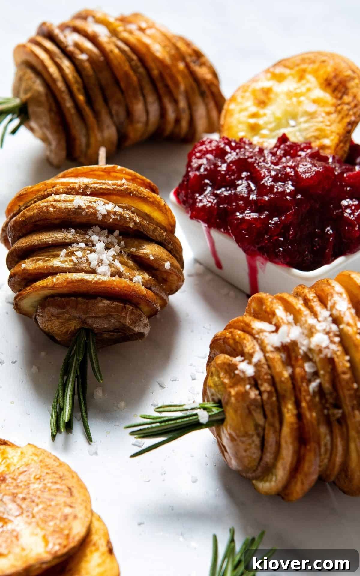 Crispy roasted potato slices shaped like Christmas trees, arranged around a small bowl of vibrant red cranberry sauce, garnished with rosemary.