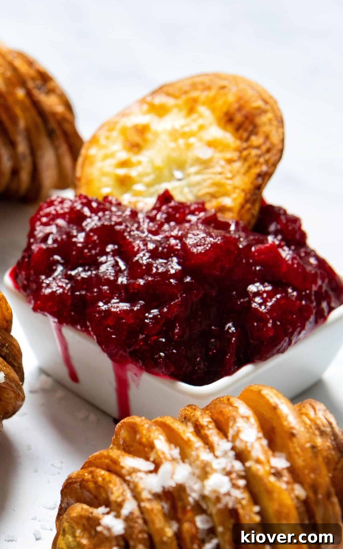 A crispy roasted potato slice being dipped into a bowl of homemade sugar-free cranberry sauce, showcasing the sauce's texture and color.