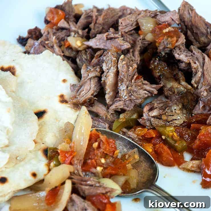 Succulent shredded beef on a wooden cutting board, surrounded by fresh lime wedges, cilantro, onions, and warm flour tortillas, ready for authentic Mexican meals.