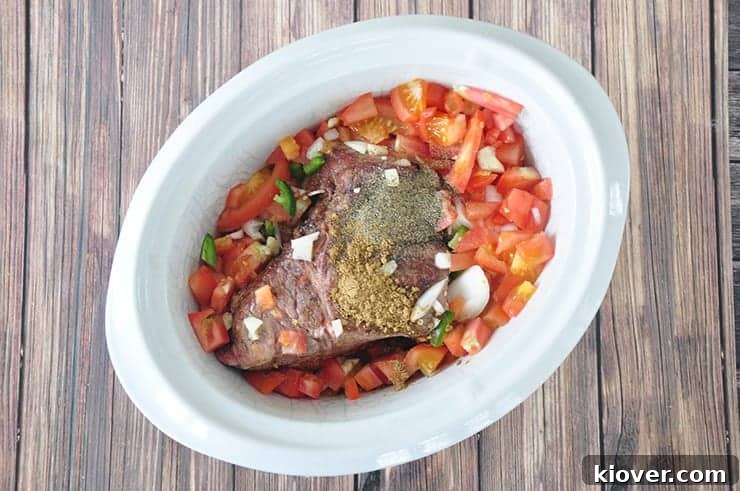 A robust beef chuck roast nestled in a slow cooker, surrounded by fresh diced tomatoes, chopped onions, and sliced jalapenos, ready to begin its long, slow simmer.
