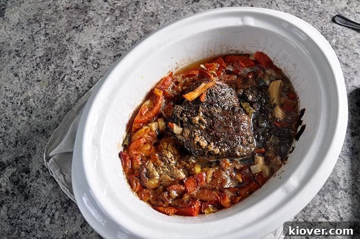 The fully cooked beef roast rests in the slow cooker, its fibers visibly tender and ready to be effortlessly pulled apart for a delicious shredded beef dish.