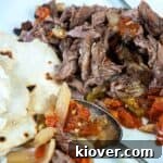 Shredded beef on a cutting board with some of the fixings and flour tortilla on the side