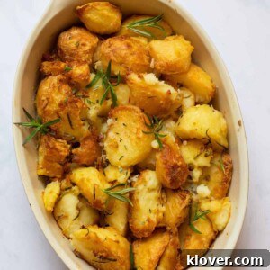 Crispy golden Rosemary Roast Potatoes infused with fresh herbs, served in a rustic baking dish on a white marble surface.
