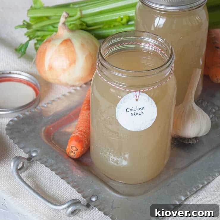 Homemade Chicken Stock in quart jars. There are onions, celery, carrots, and garlic spread around the chicken stock.