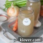Homemade Chicken Stock in quart jars. There are onions, celery, carrots, and garlic spread around the chicken stock.