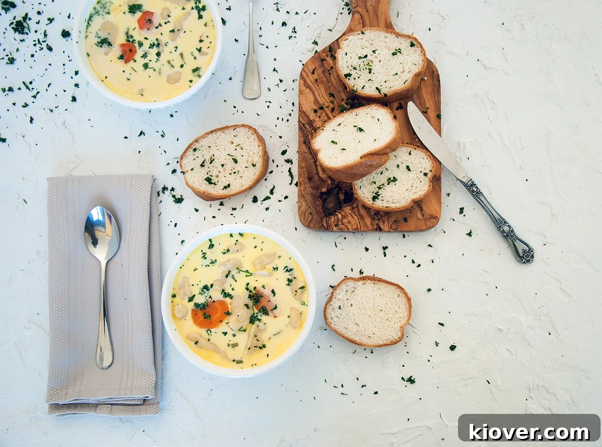 An overhead shot showcasing two inviting bowls of Knoephla Soup, accompanied by a wooden cutting board with sliced French bread.