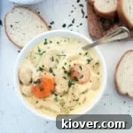 A bowl of Knoephla Soup with parsley sprinkled on top and french bread in the background.