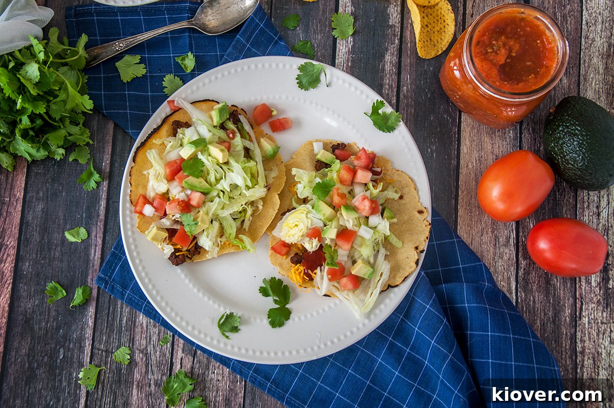 Holding one of two tacos over a plate. The plate is on a table that contain a bunch of taco fixings.