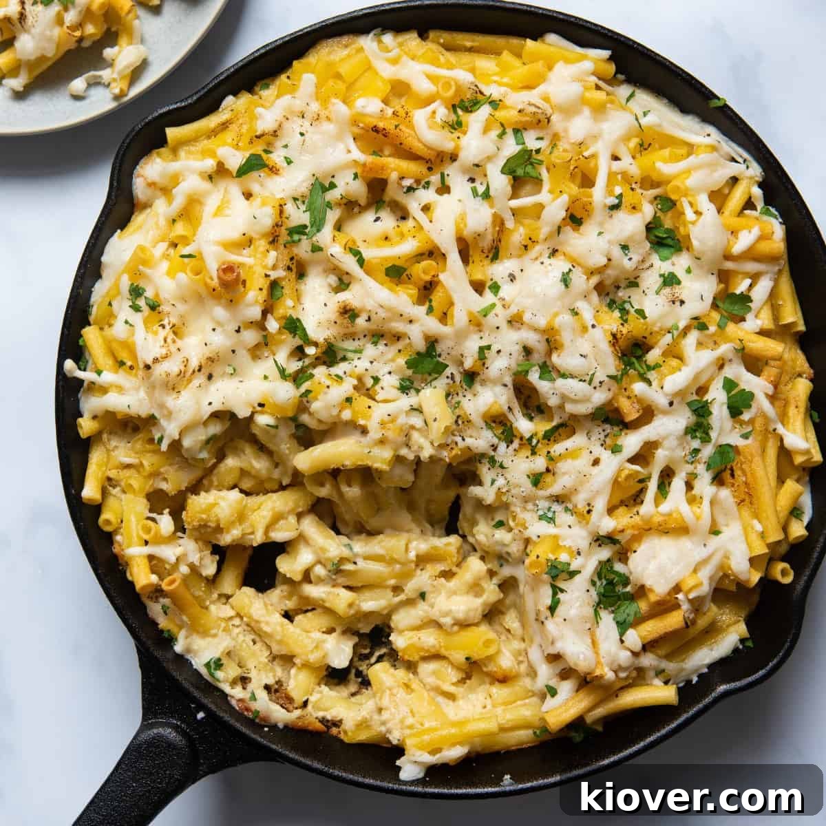 An inviting overhead shot of creamy vegan mac and cheese served in a rustic black skillet pan, presented on a clean white background, highlighting its rich texture and golden topping.