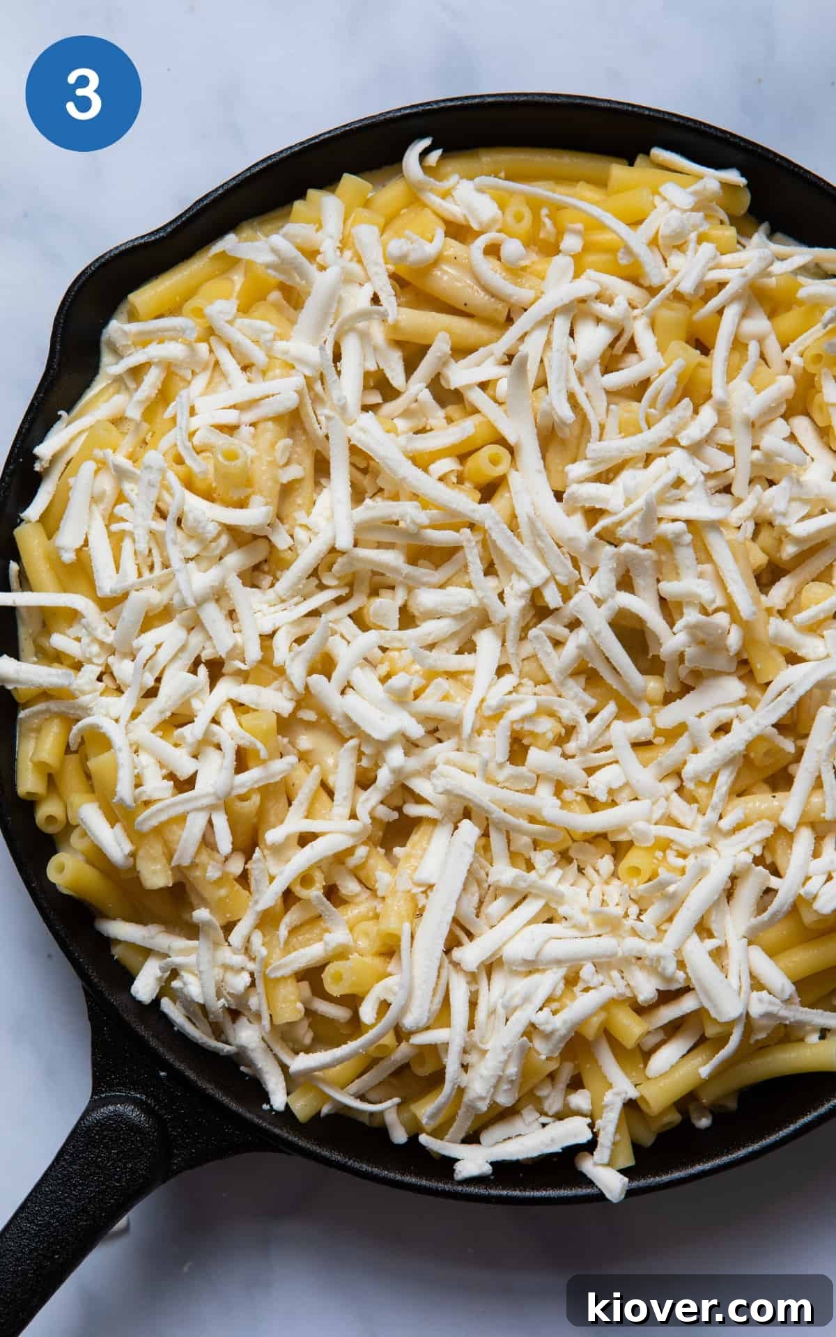 A black skillet pan filled with vegan mac and cheese, generously topped with shredded vegan cheddar cheese, prepared for baking to achieve a golden crust.