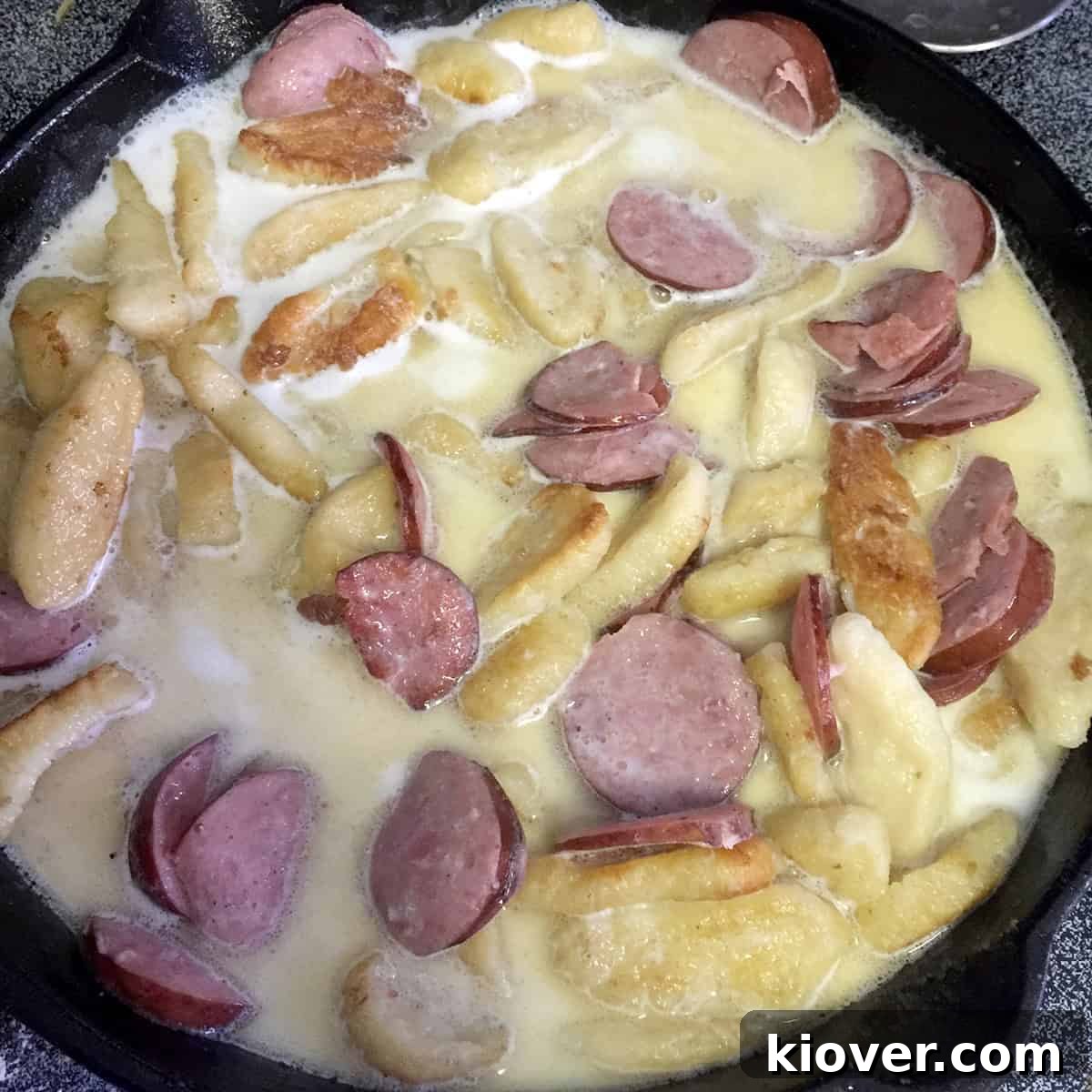A skillet of sausage and knoephla mix being brought to a gentle simmer with milk.