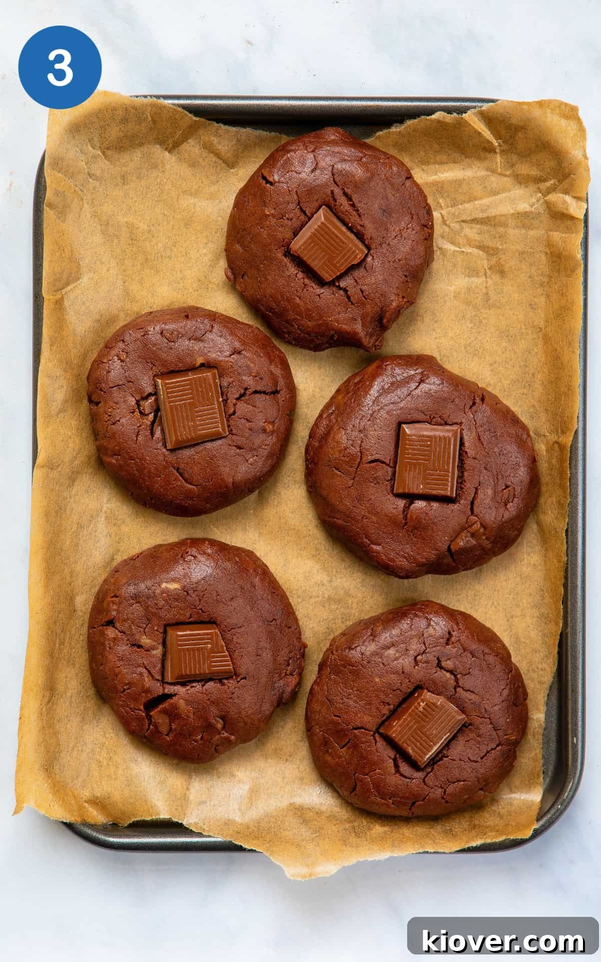 Decadent Gluten-Free Chocolate Treats 6 Formed gluten-free chocolate cookies, topped with chocolate chunks, arranged on a lined baking tray ready for the oven.