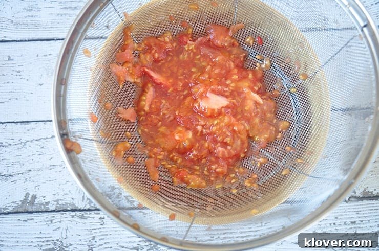 Tomato seeds and pulp straining into a bowl, demonstrating the separation process.