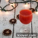 A glass of homemade tomato juice on a wood table with dried limes and holiday lights in the background