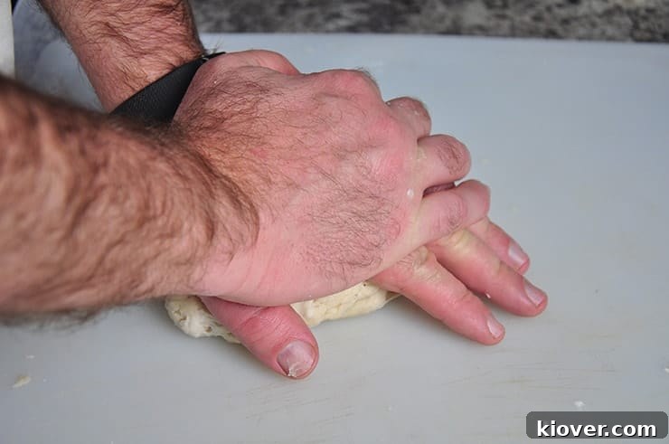 A hand gently pressing down on a ball of flour tortilla dough, beginning the flattening process.