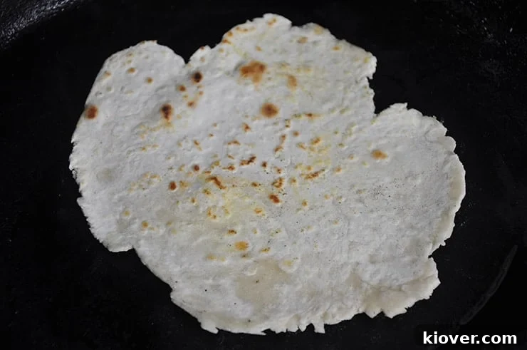 A freshly cooked flour tortilla sizzling on a cast iron pan, showing light browning and bubbling.