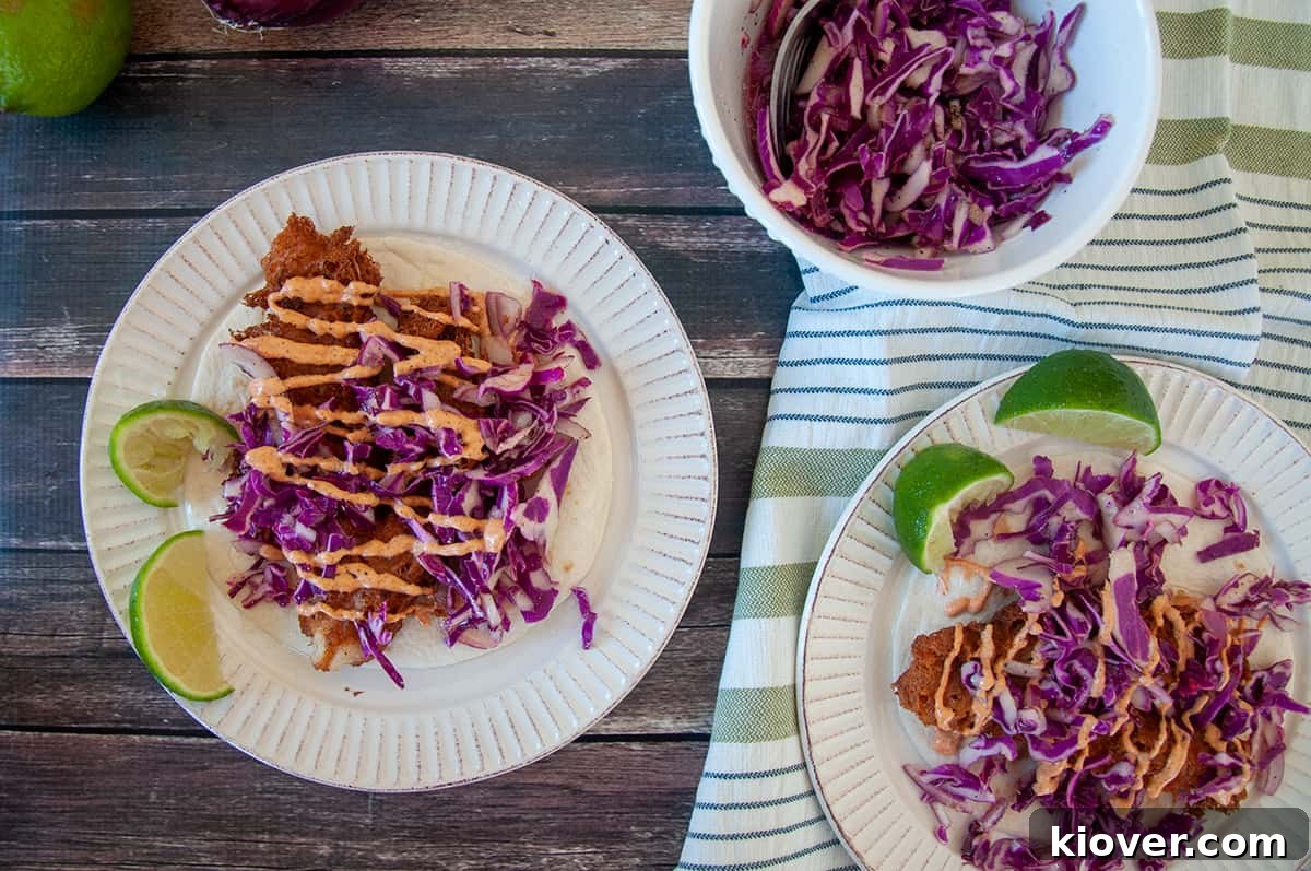 Two fish tacos beautifully arranged on white plates with lime wedges on the side.