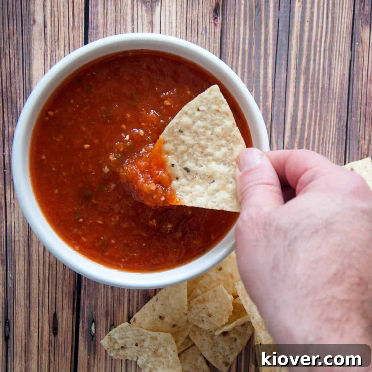 A hand dipping chips into our homemade salsa in a white bowl.