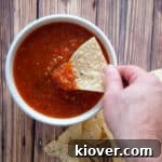 A hand dipping chips into our homemade salsa in a white bowl.