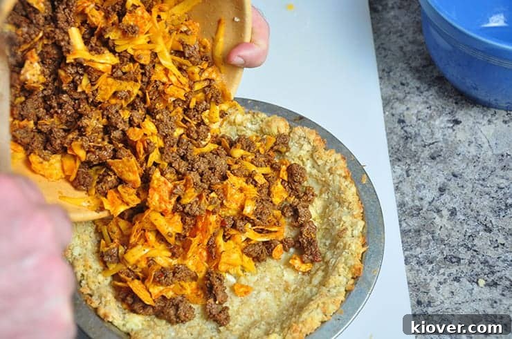 Pouring beef Dorito mixture into tater tot pie crust.