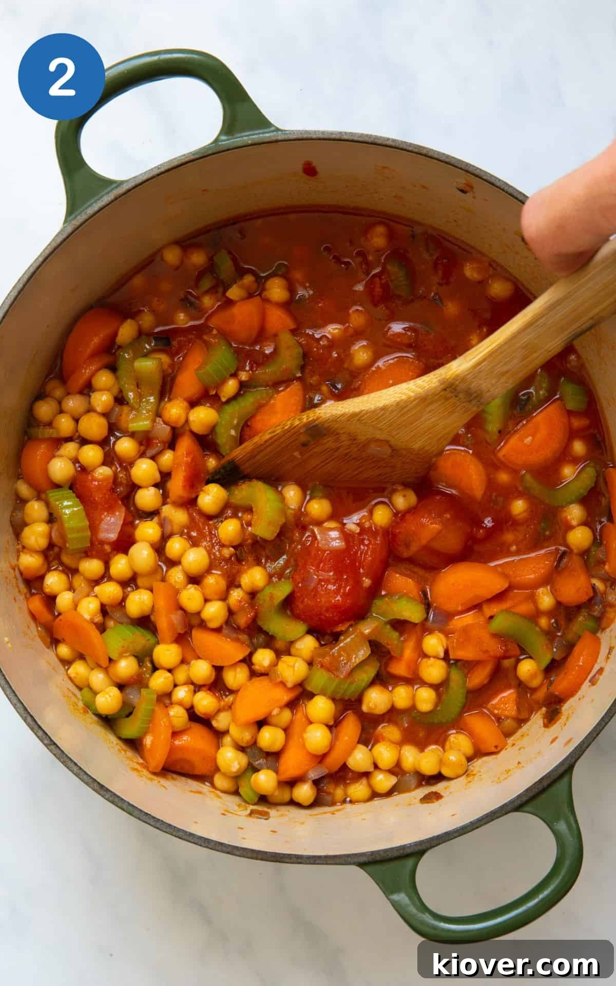 All the vibrant ingredients for the chickpea stew, including spices, chickpeas, tinned tomatoes, and vegetable stock, are combined in a large pot and stirred, ready to simmer and thicken.
