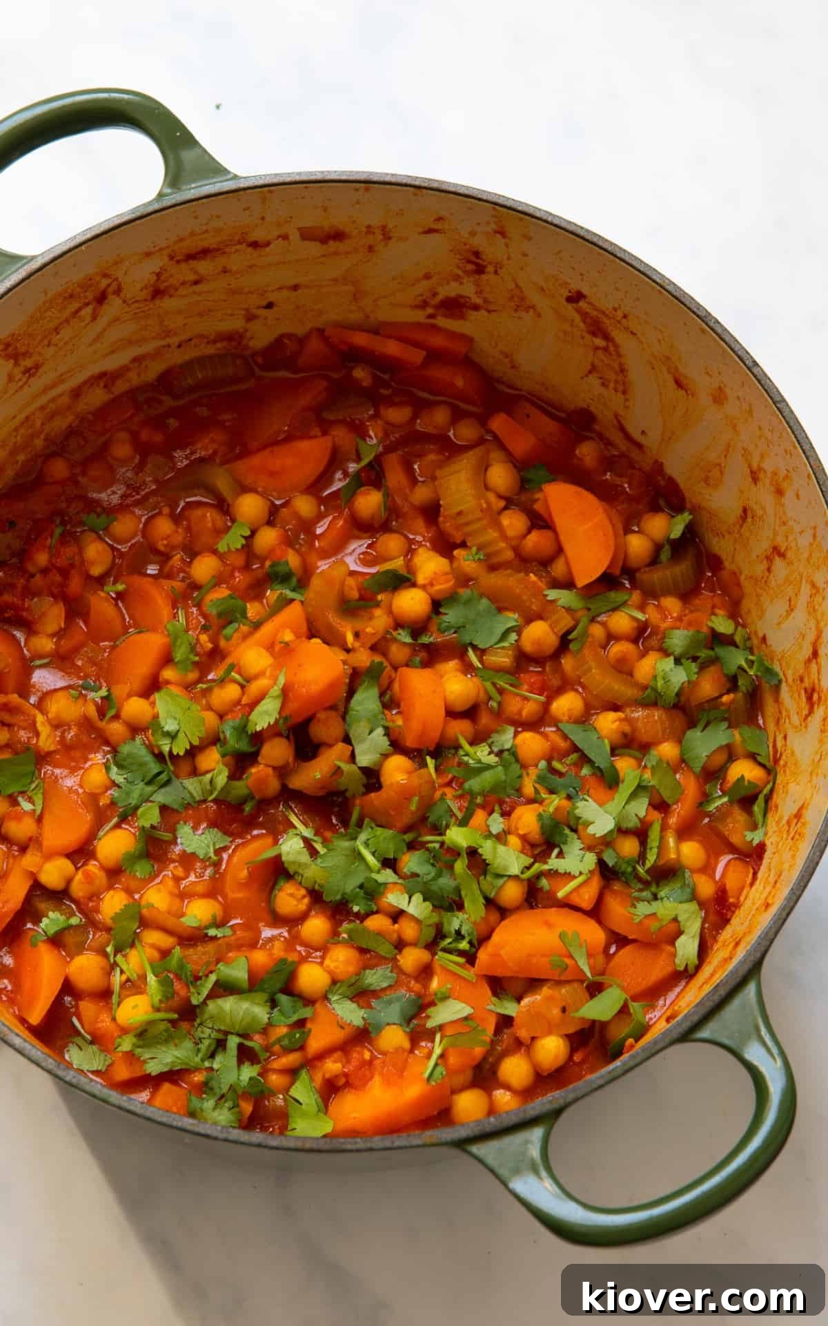 A large pot of vibrant sweet potato stew, garnished with fresh herbs, is displayed on a rustic white surface, invitingly ready to be served.