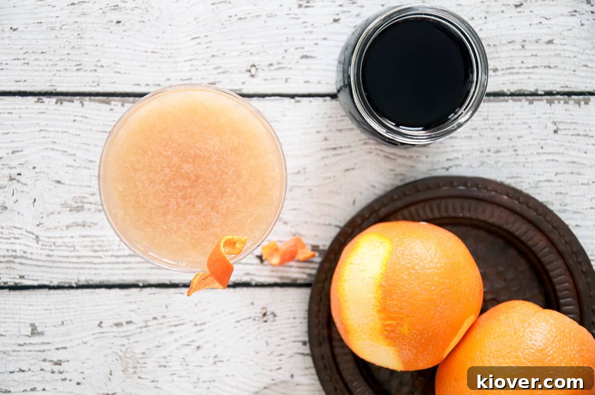 An overhead shot of a beautifully prepared Monkey Gland cocktail, featuring its signature red hue from grenadine and a vibrant orange twist garnish, placed alongside fresh orange slices.