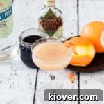 A picture of one Monkey Gland cocktail with gin, grenadine, oranges, and absinthe in the background.