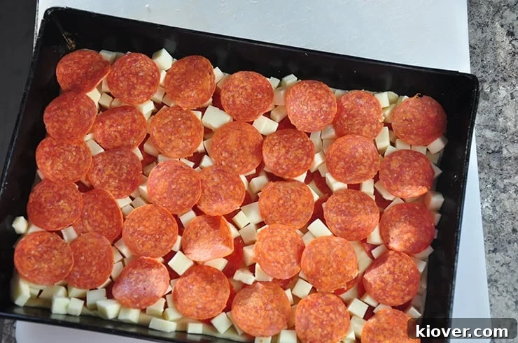 Detroit Style Pizza dough in pan, topped generously with cubed mozzarella cheese and scattered pepperoni, awaiting the final sauce application.
