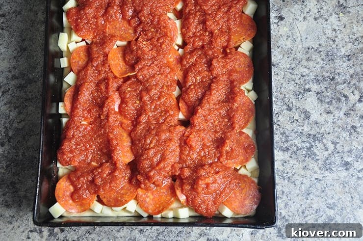 Uncooked Detroit Style Pizza in its pan, beautifully topped with cheese, pepperoni, and three distinctive stripes of rich red sauce, ready for the oven.