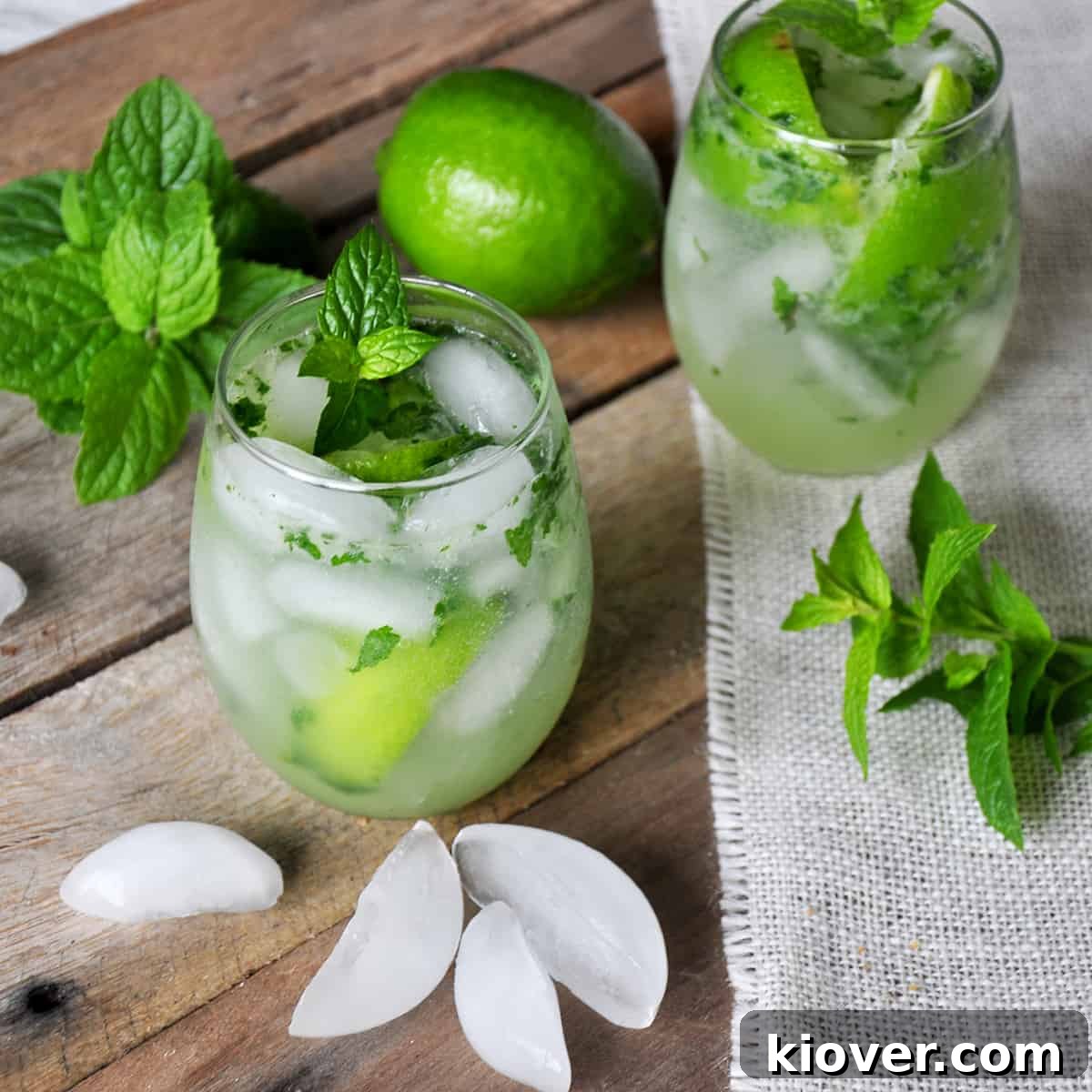 Mojito on a picnic table with mint, ice, and a whole lime.