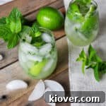 Mojito on a picnic table with mint, ice, and a whole lime.