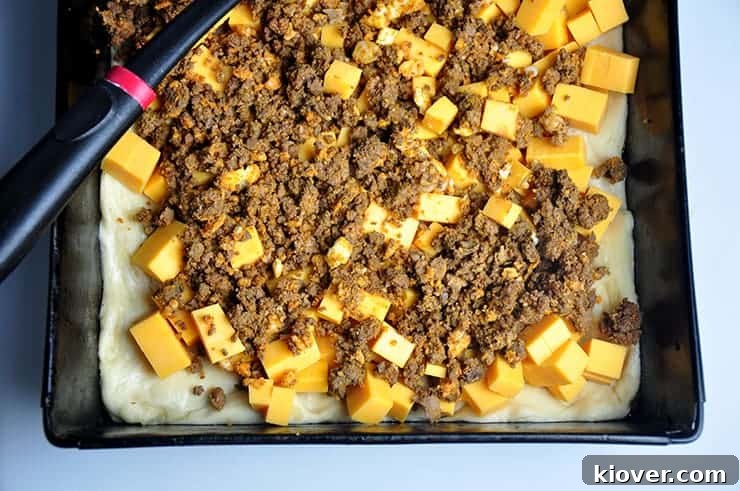 Uncooked Detroit Style Coney Island pizza dough layered with rich, savory ground meat and cheddar cheese cubes, awaiting its transformation in the oven.