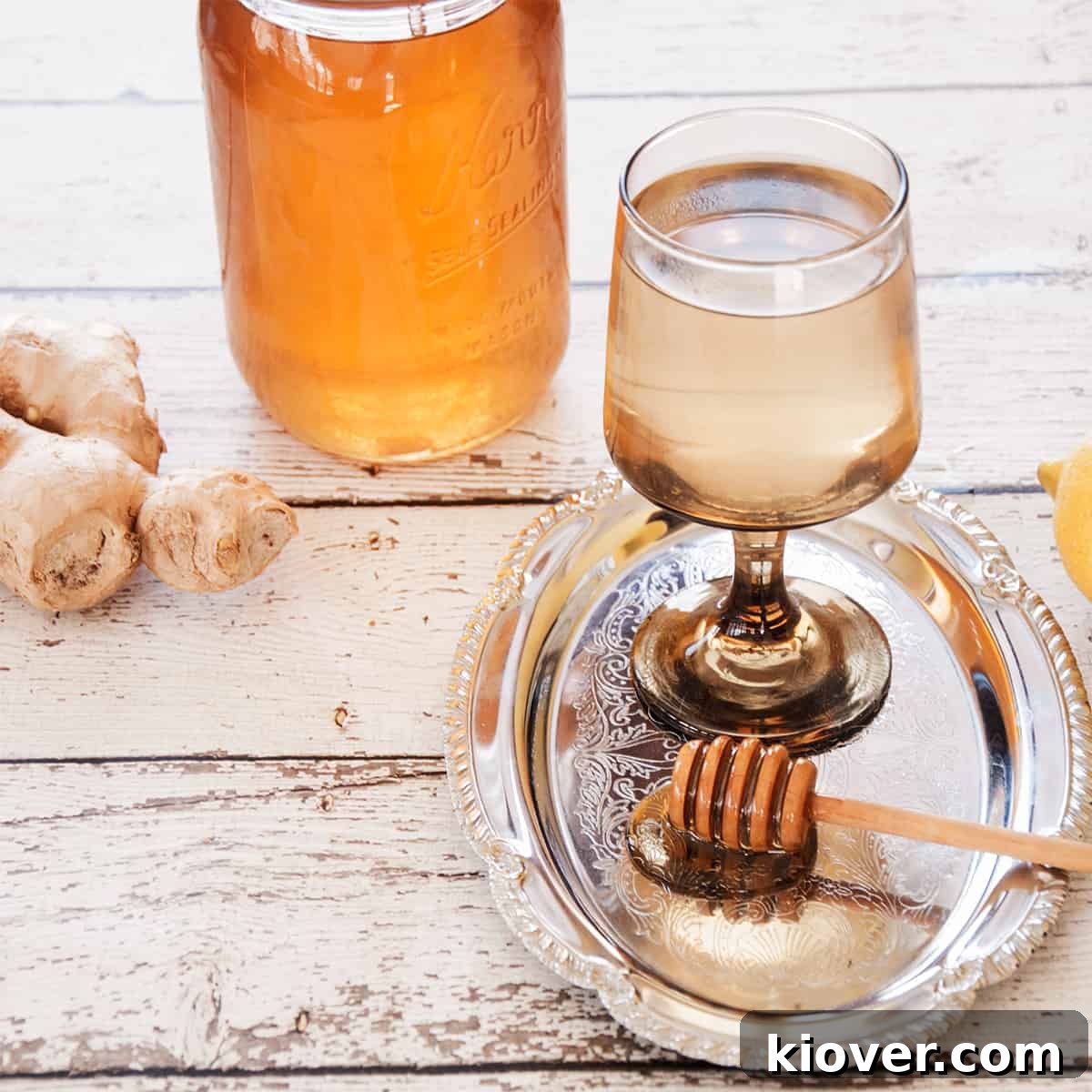 A glass of hot ginger tea with a bit of honey dipper covered with honey and ginger in the background, set against a rustic backdrop.