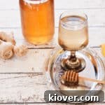A glass of hot ginger tea with a bit of honey dipper covered with honey and ginger in the background.