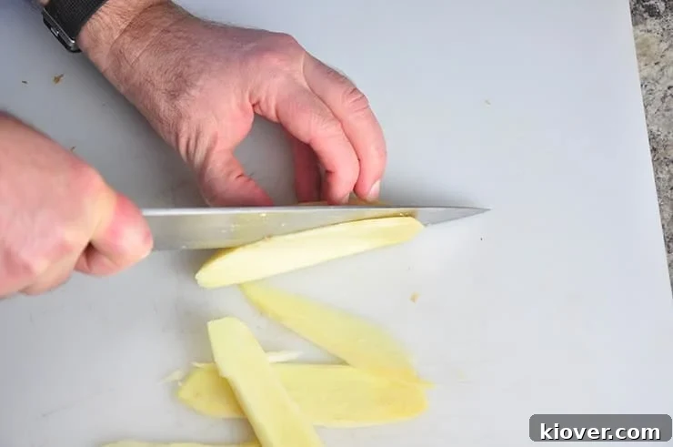 Close-up of fresh ginger root being thinly sliced on a wooden cutting board with a sharp knife, preparing it for the candying process.
