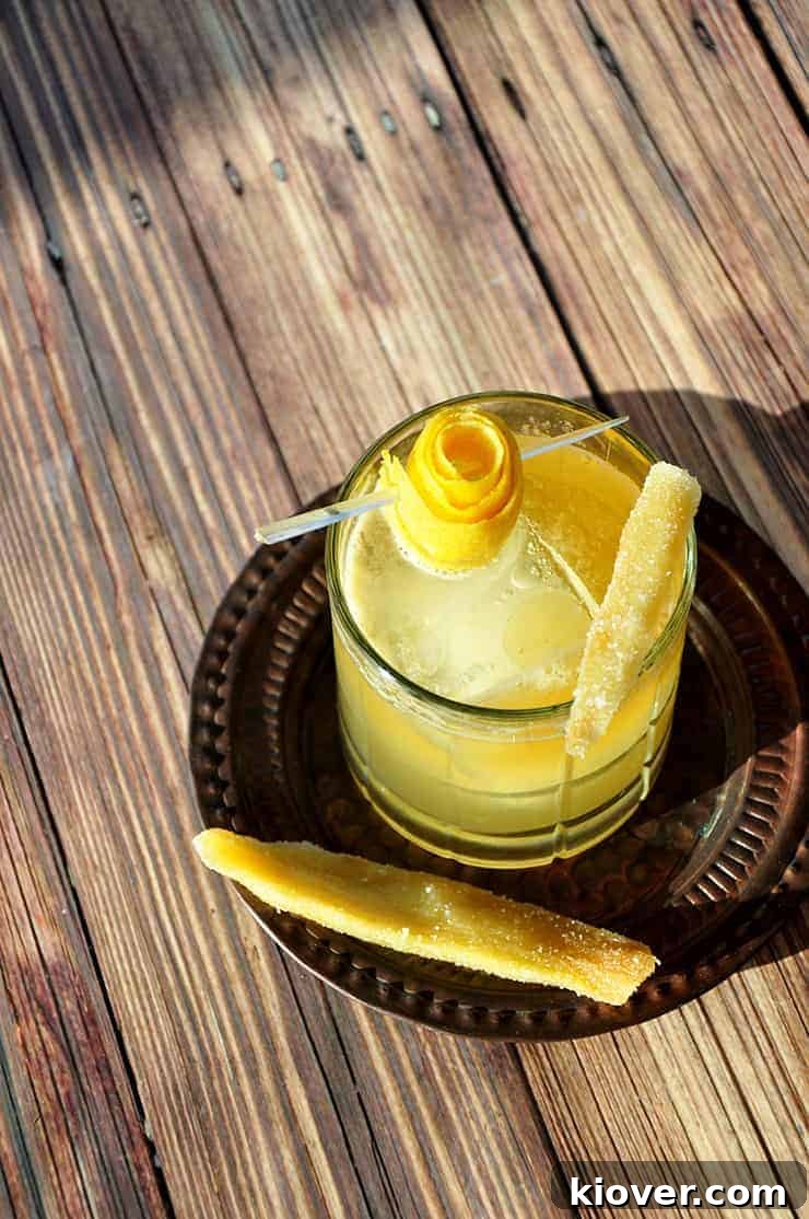 A Penicillin Cocktail on a serving trey, garnished with a lemon and 2 pieces of candied ginger.