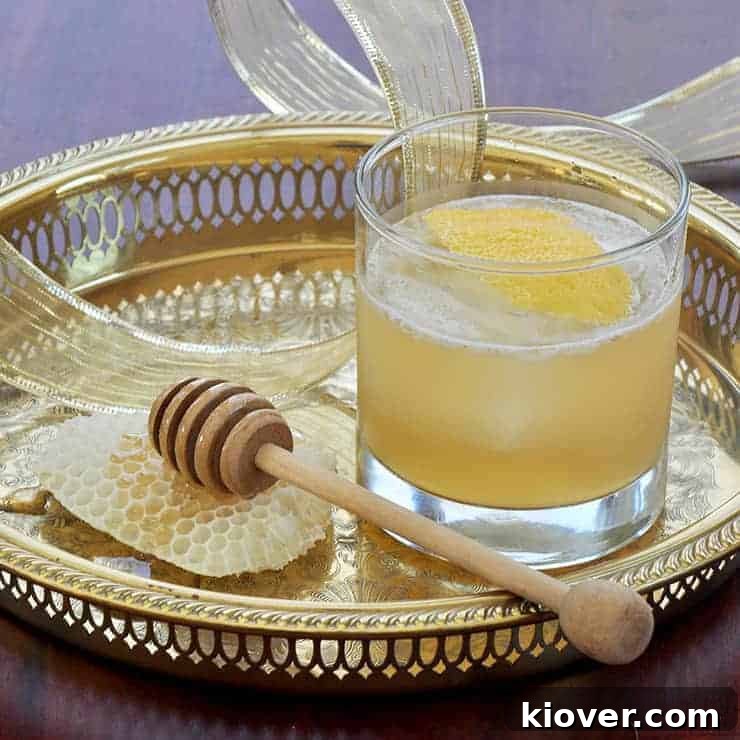 Gold Rush Cocktail on a Gold Platter with honey and a honey dipper to the side