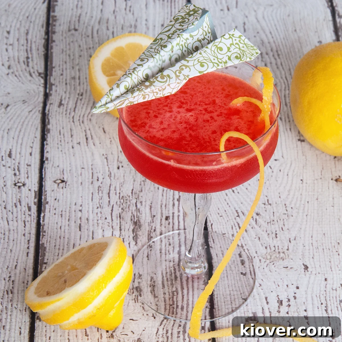 Paper Plane Cocktail with a long lemon twist and lemons in the background.