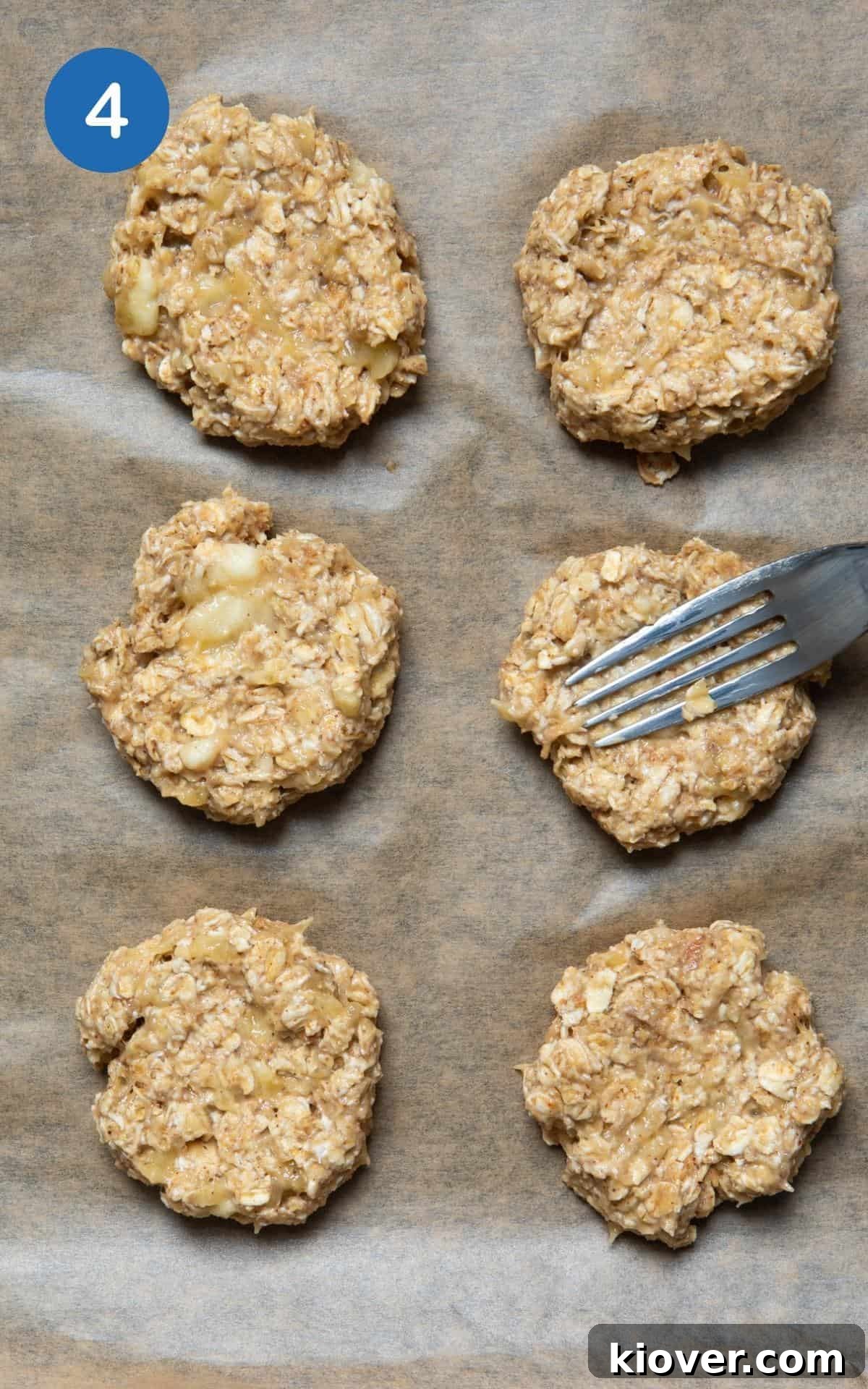 Formed oat cookies laid out on a baking tray with parchment paper, each pressed down with a fork to create a classic cookie shape.