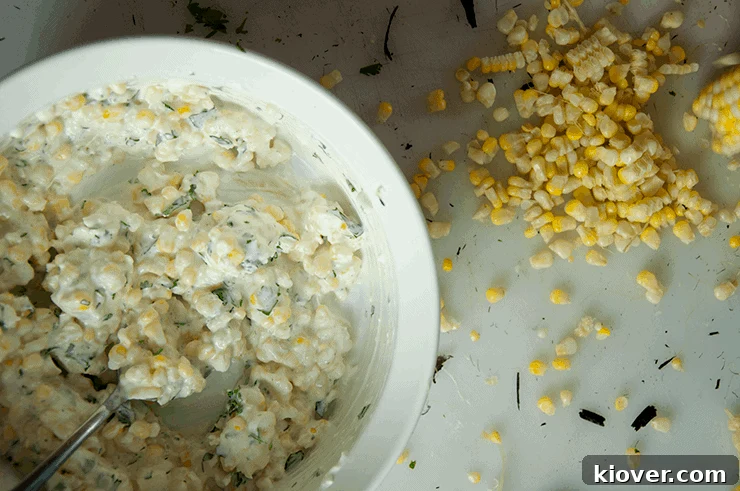 All ingredients for the Mexican corn sauce being thoroughly mixed together in a white bowl, showcasing the creamy texture.