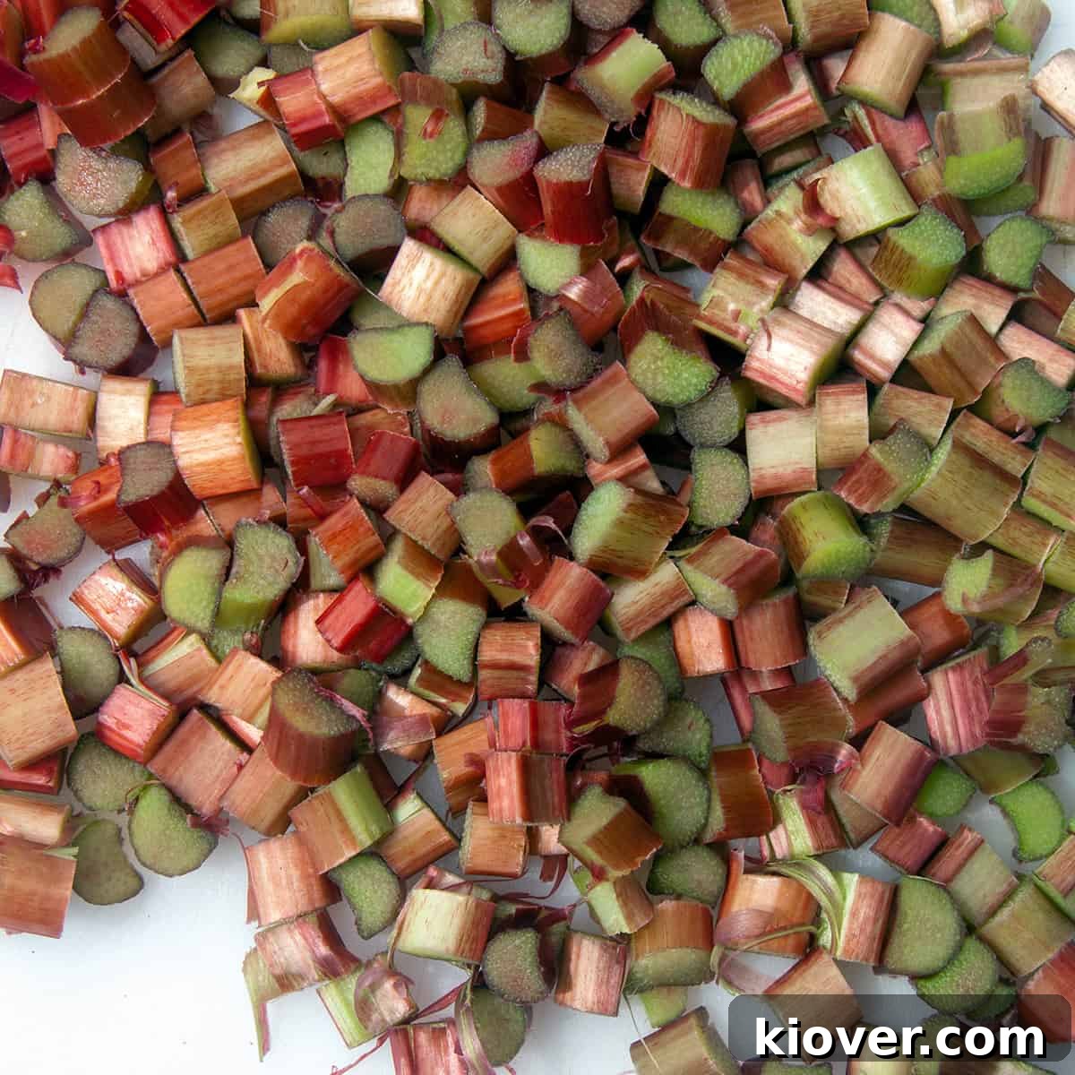 Freshly chopped raw rhubarb stalks on a white plate, ready for syrup preparation.