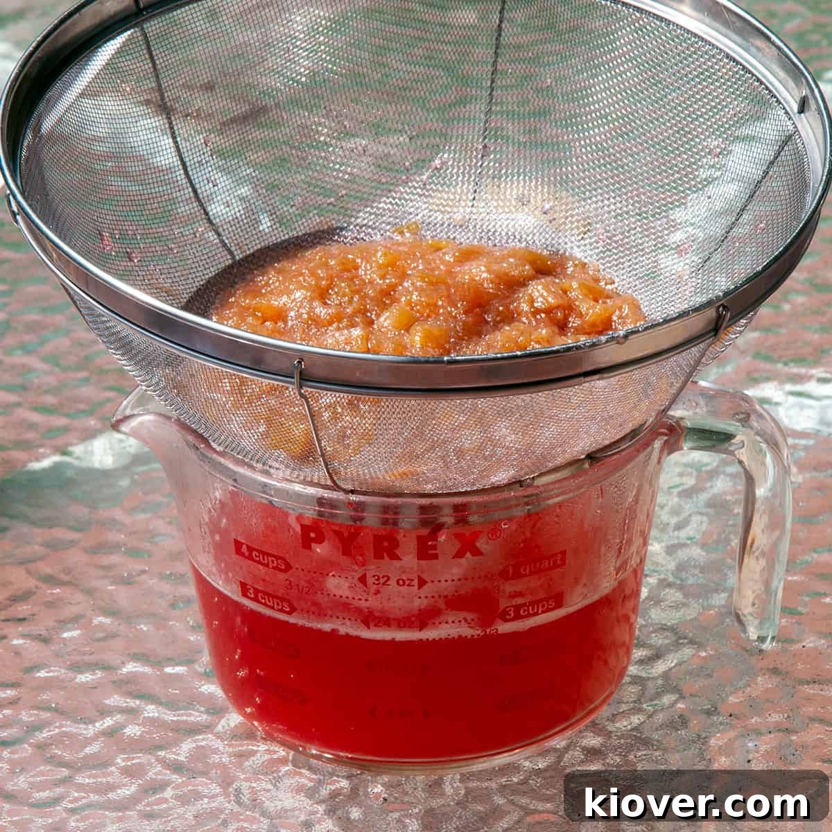 A fine mesh strainer being used to separate the vibrant pink rhubarb syrup from the cooked rhubarb solids.