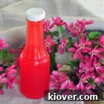 Rhubarb Syrup in a bottle on a picnic table with flowers laying around.