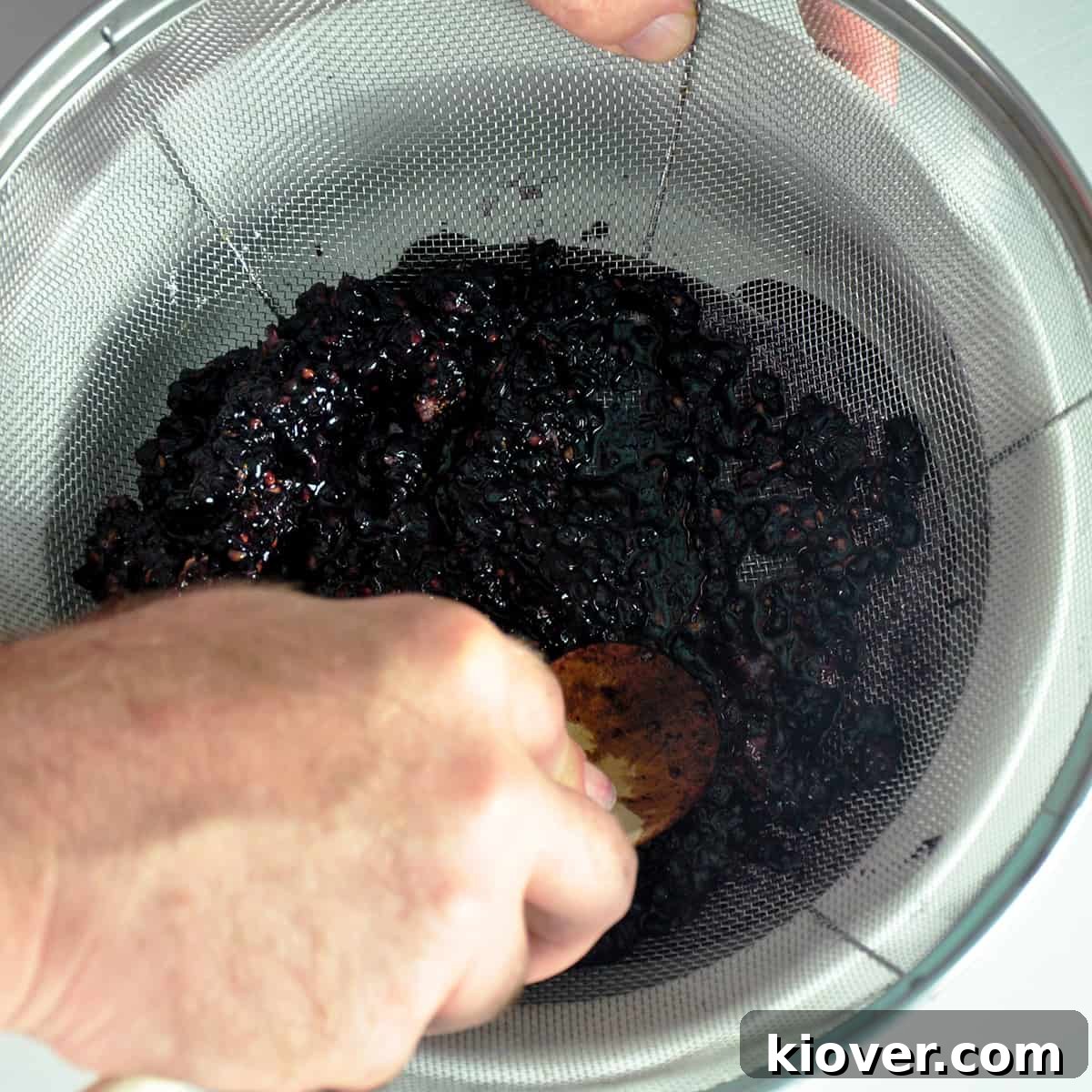 A hand pressing blackberry juice through a fine mesh strainer.