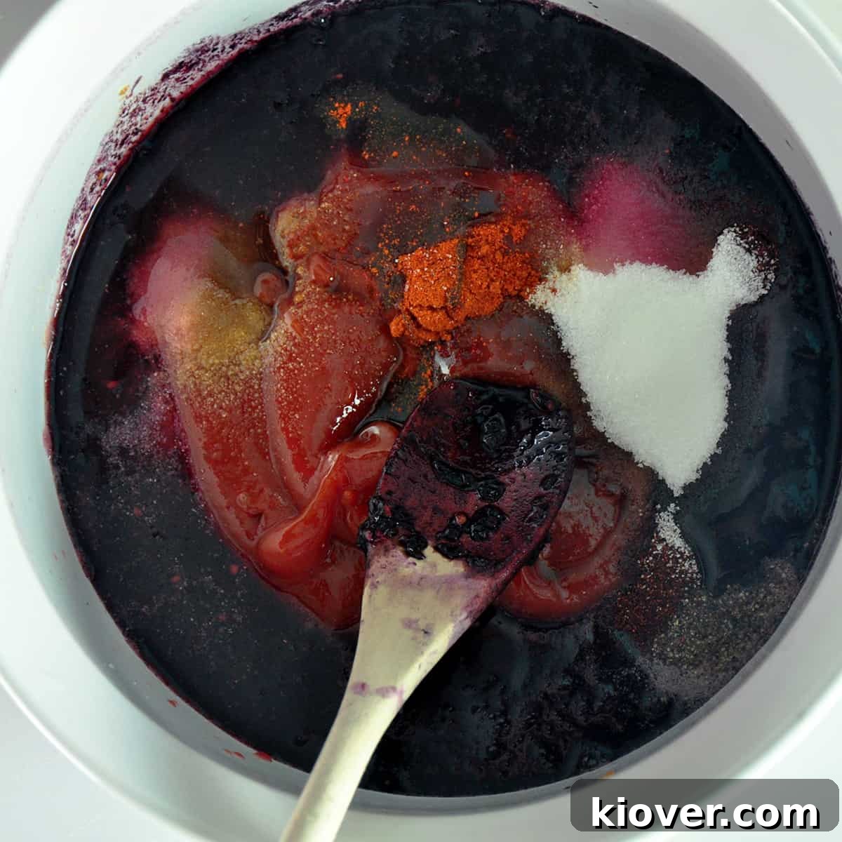 A wooden spoon with Blackberry BBQ sauce in a white bowl.